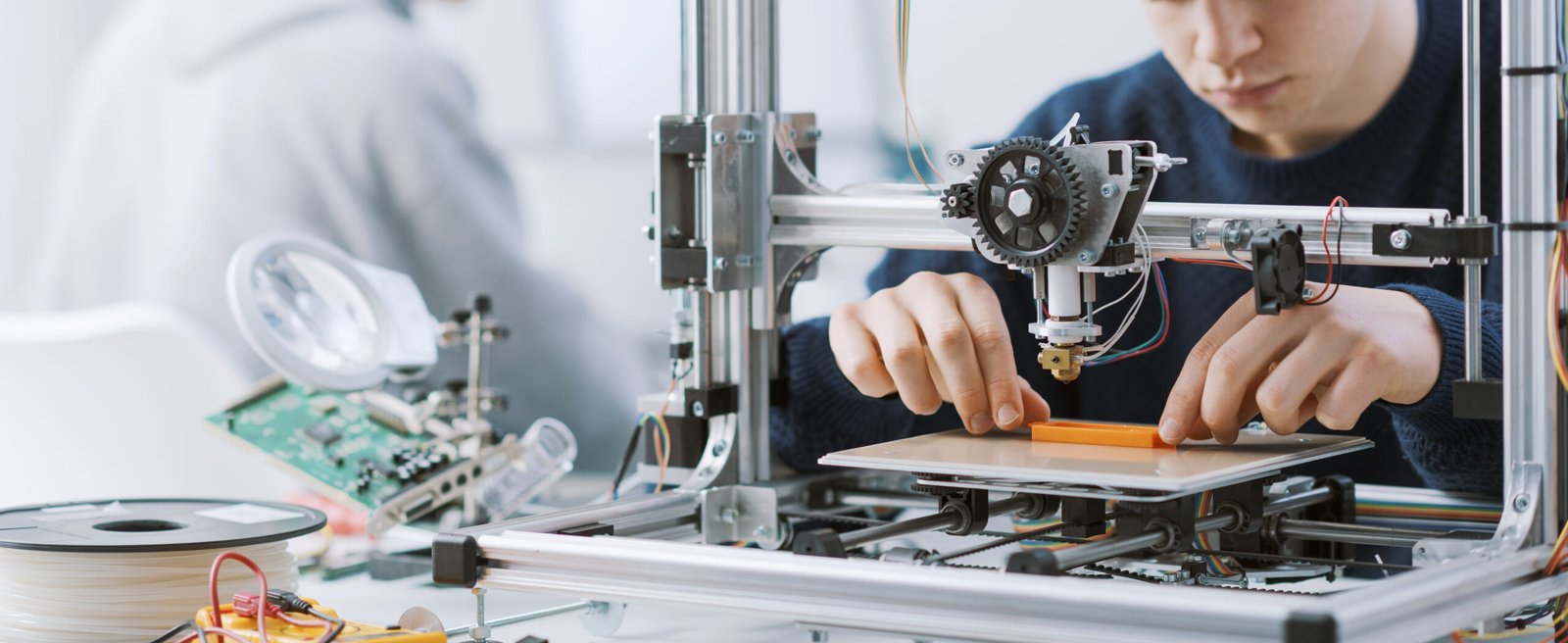 Young smart student working with a 3D printer in the lab, he is printing a prototype